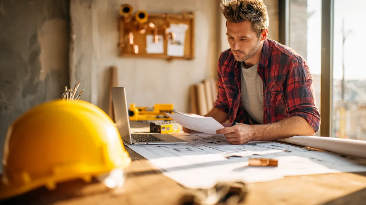 Artisan sur chantier vérifiant les délais de paiement sur laptop